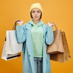 Stylish woman in colorful outfit holding multiple shopping bags against a vibrant yellow background.
