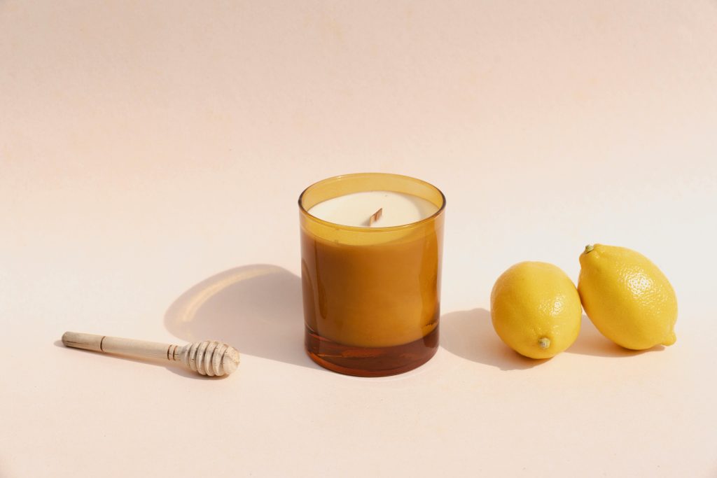 Warm candle with fresh lemons and honey dipper on a soft background, evoking citrus freshness.