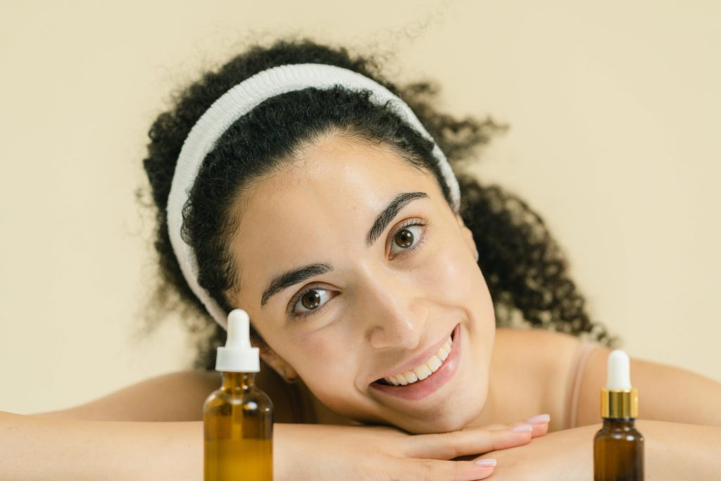 pexels photo 9775407 9775407 Woman with curly hair smiling, showcasing skincare products, indoors.